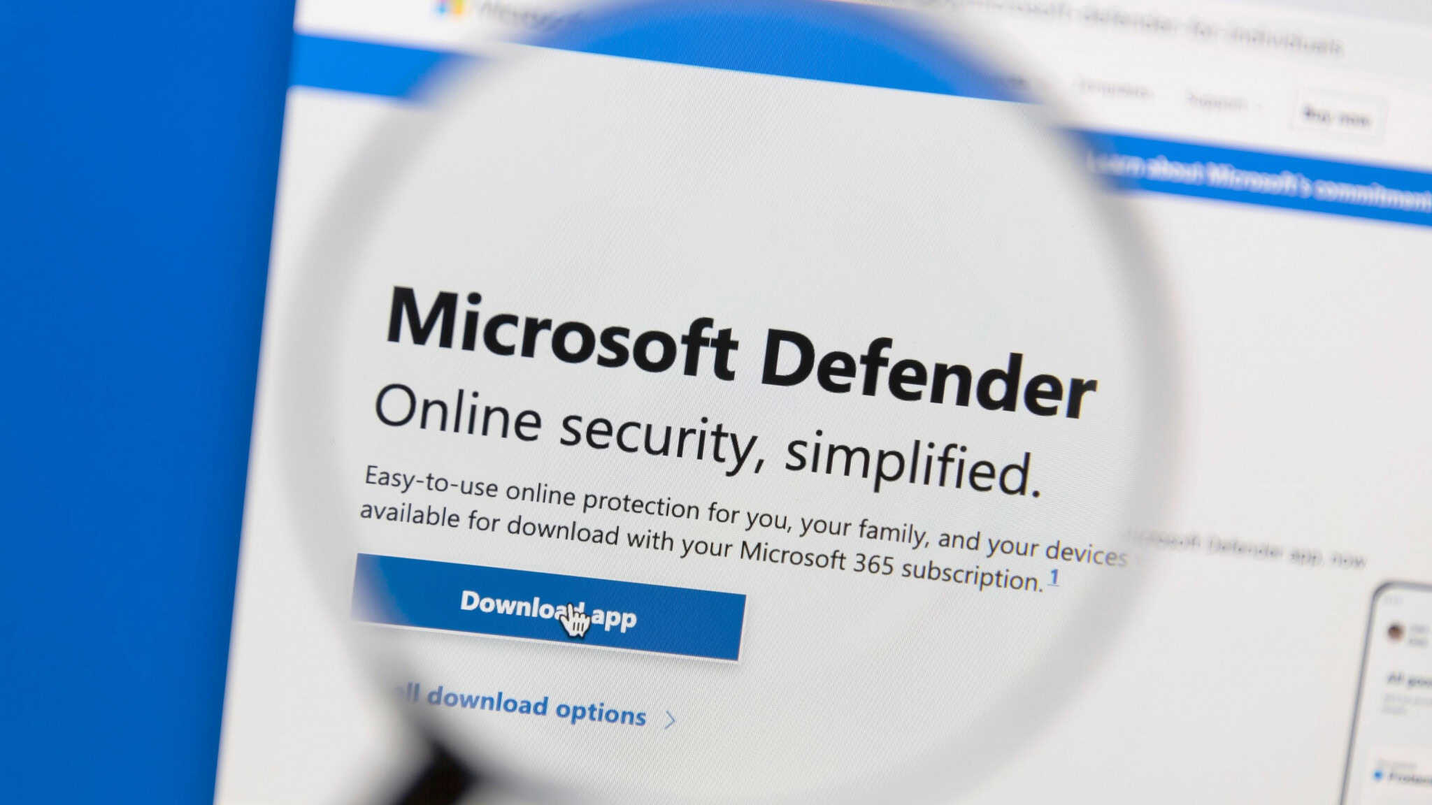 Tela de computador mostra o site do Microsoft Defender com uma lupa destacando o texto “Segurança online simplificada” e botão “Download APP”.